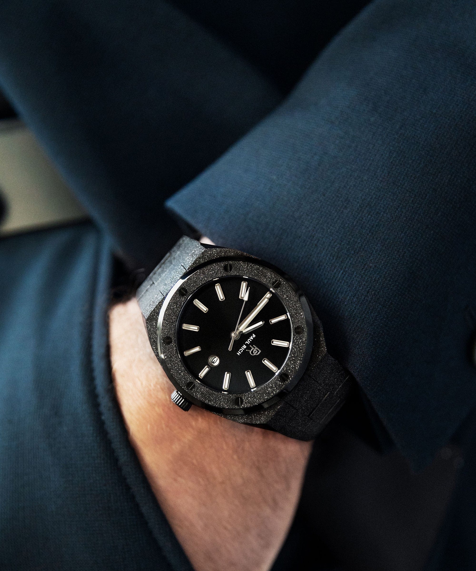 Paul Rich frosted black watch with sunray dial and silver markers, worn on wrist with dark blazer, close-up view.